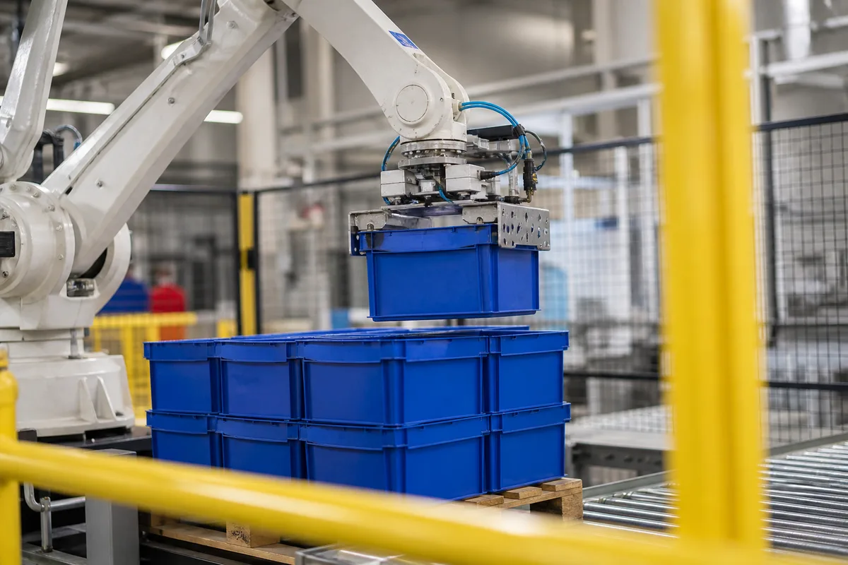 Bras robotisé blanc palettisant des caisses plastiques sur un convoyeur en acier inoxydable